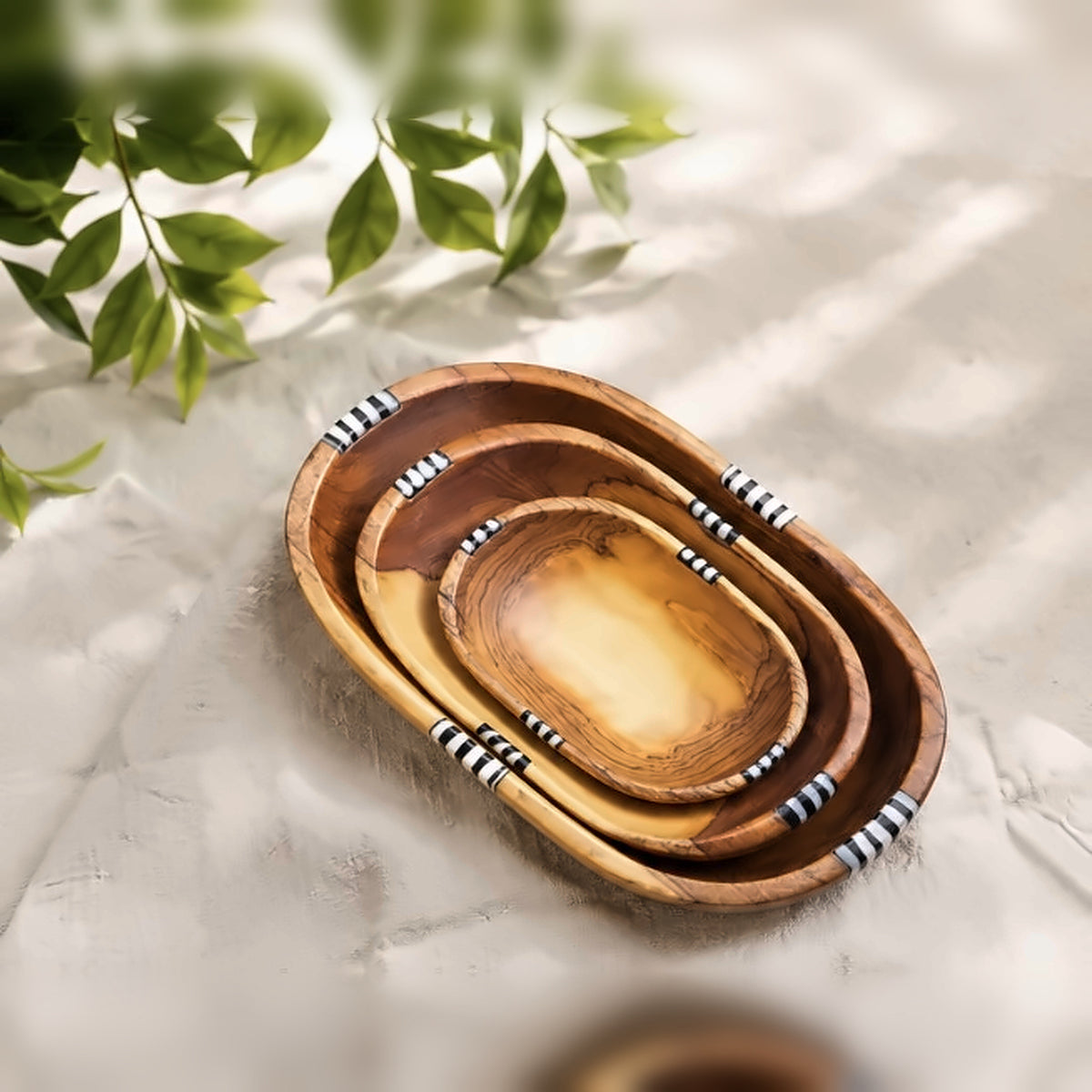Three hand-carved olive wood nesting bowls with batik bone inlay, resting on linen under dappled light