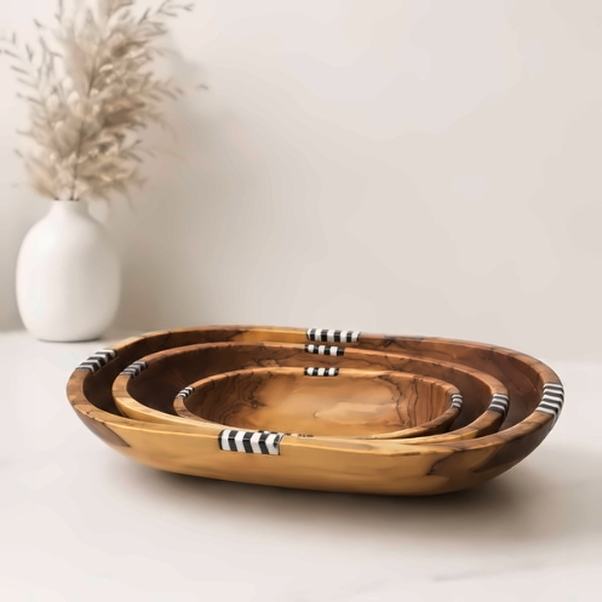 Olive wood nesting bowls on marble beside a white ceramic vase holding dried pampas grass
