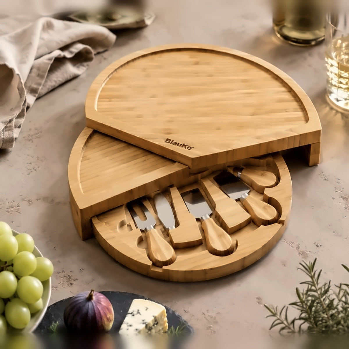 Swiveling bamboo cheese board opened out with its four knives in the drawer, served with green grapes, figs and blue cheese