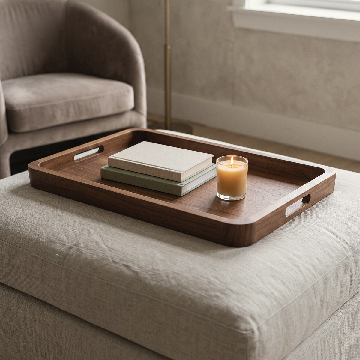 Large acacia serving tray with handles on an ottoman with books and a candle