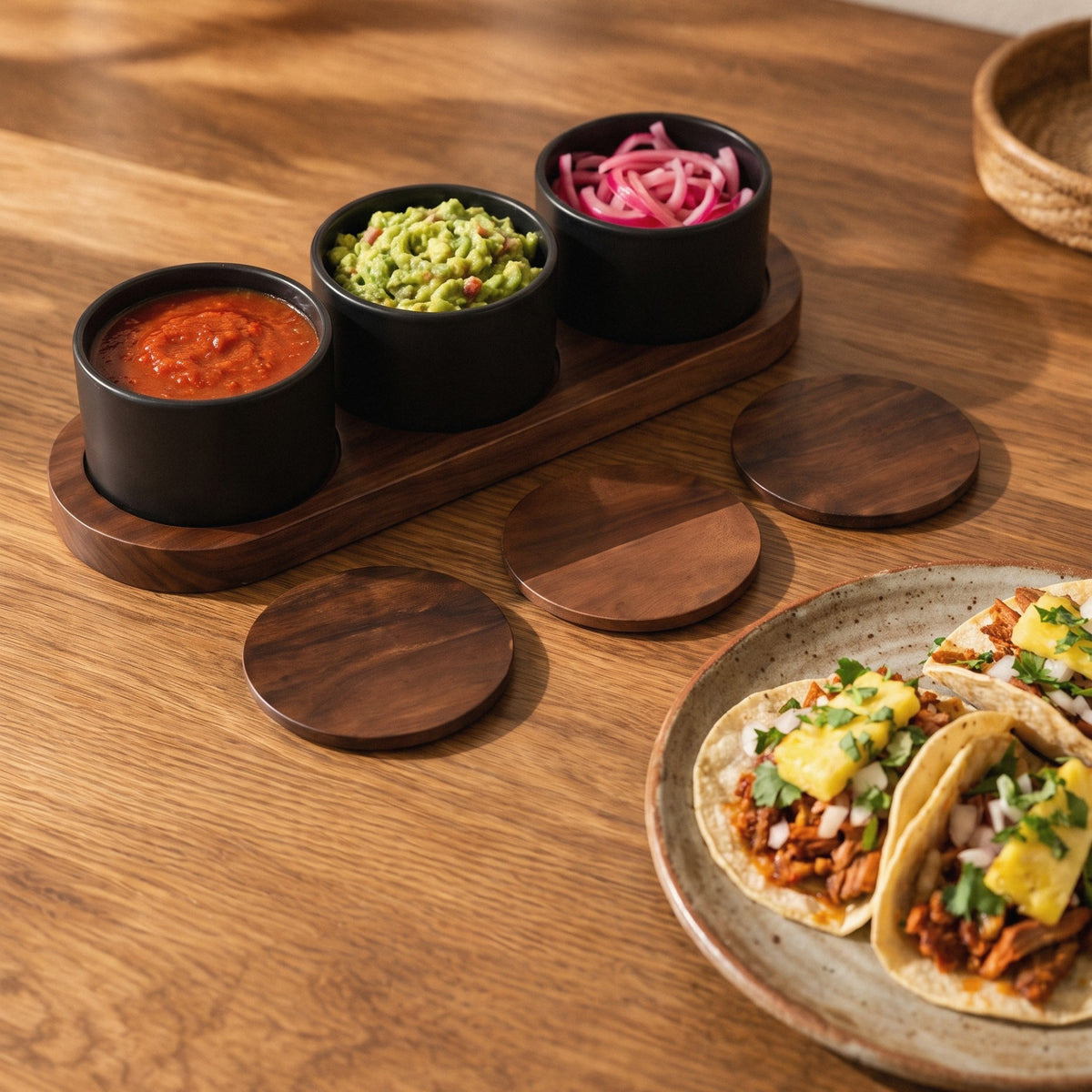 Black ceramic condiment set on acacia base with salsa, guacamole and pickled onions beside tacos