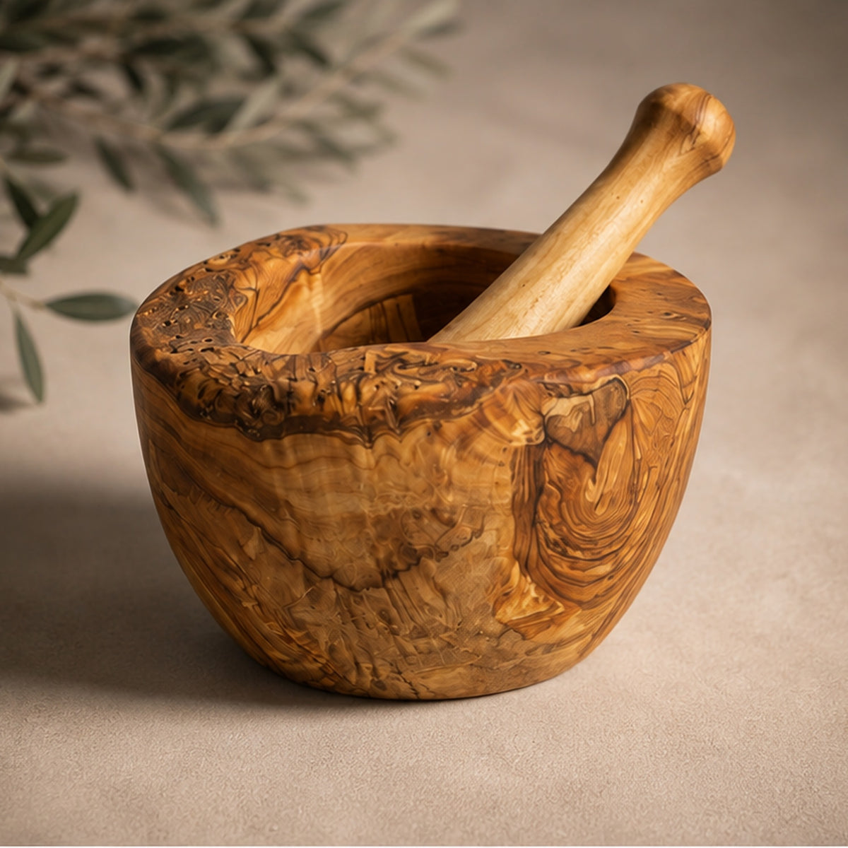 Olive wood mortar and pestle on a beige surface, with an olive branch behind it