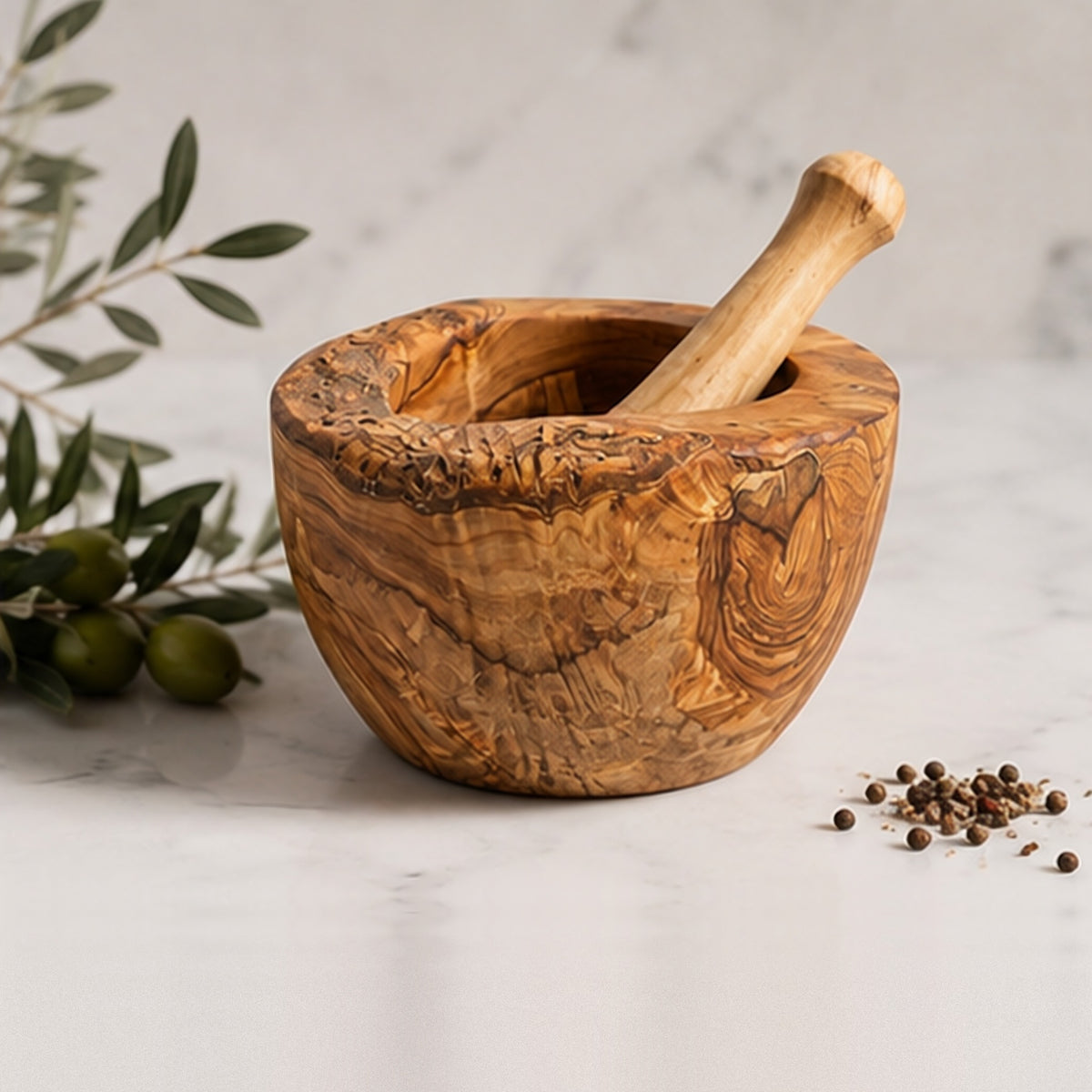 Olive wood mortar and pestle on a marble counter, with green olives and black peppercorns