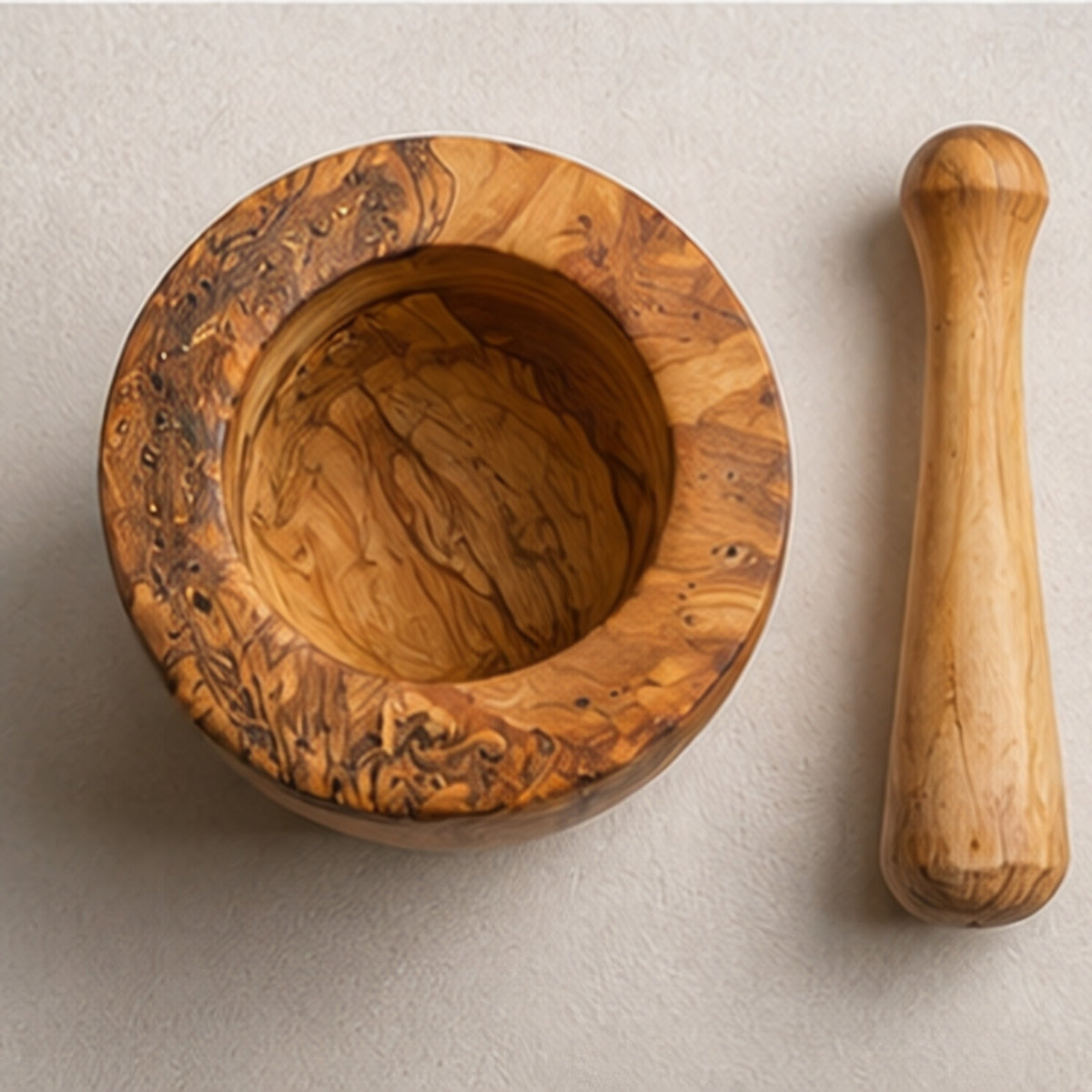 Olive wood mortar seen from above, showing the deep bowl, with the pestle laid beside it