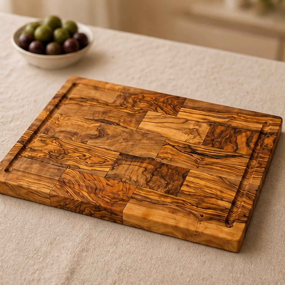Olive wood serving board on a linen tablecloth next to a small bowl of olives